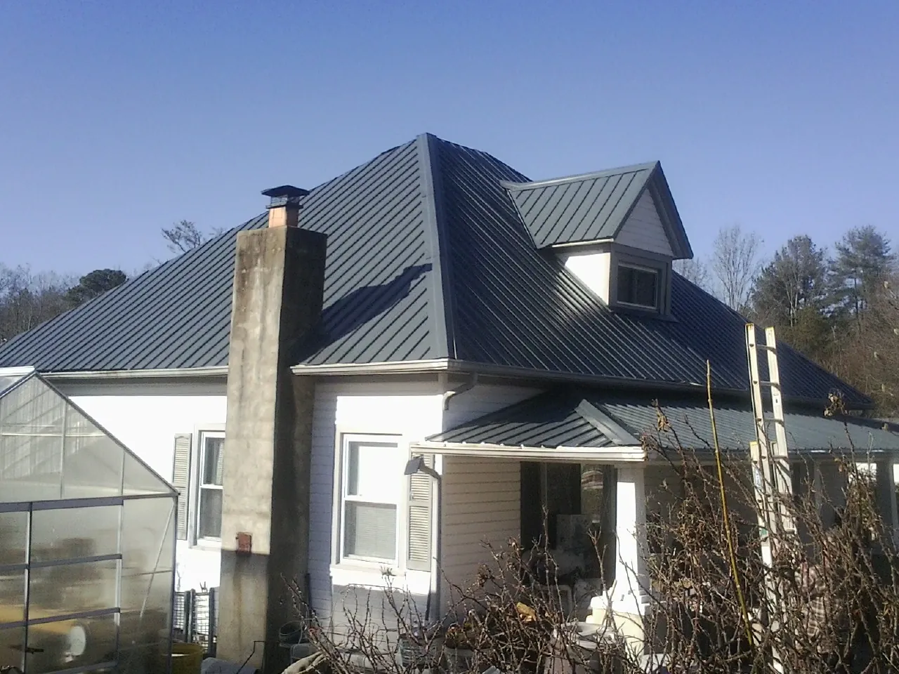 Dark blue standing seam metal roof on a white farmhouse with dormer — Slate & Tile Roof Repair by Roofing Brothers in Foosland