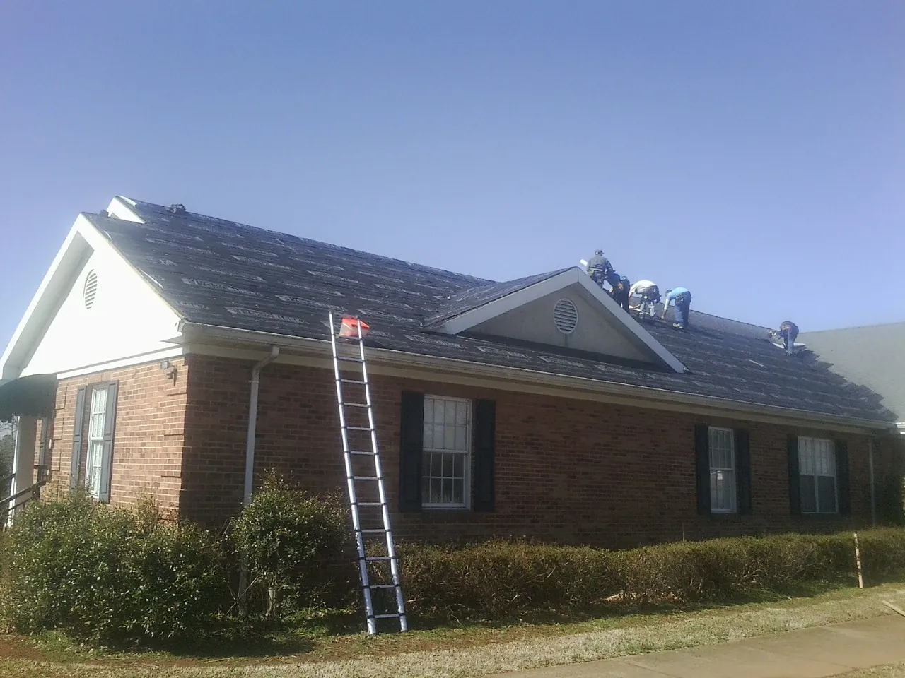 Crew tearing shingles off a brick ranch roof with a ladder set — Emergency Roof Repair work by our crew in Foosland