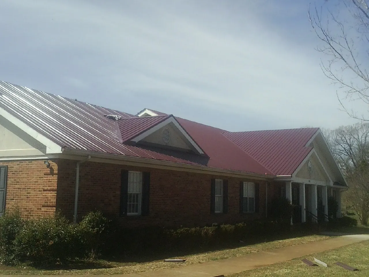 Red metal roof with gabled entries on a long brick building, from a Hail Damage Roof Repair job in Foosland
