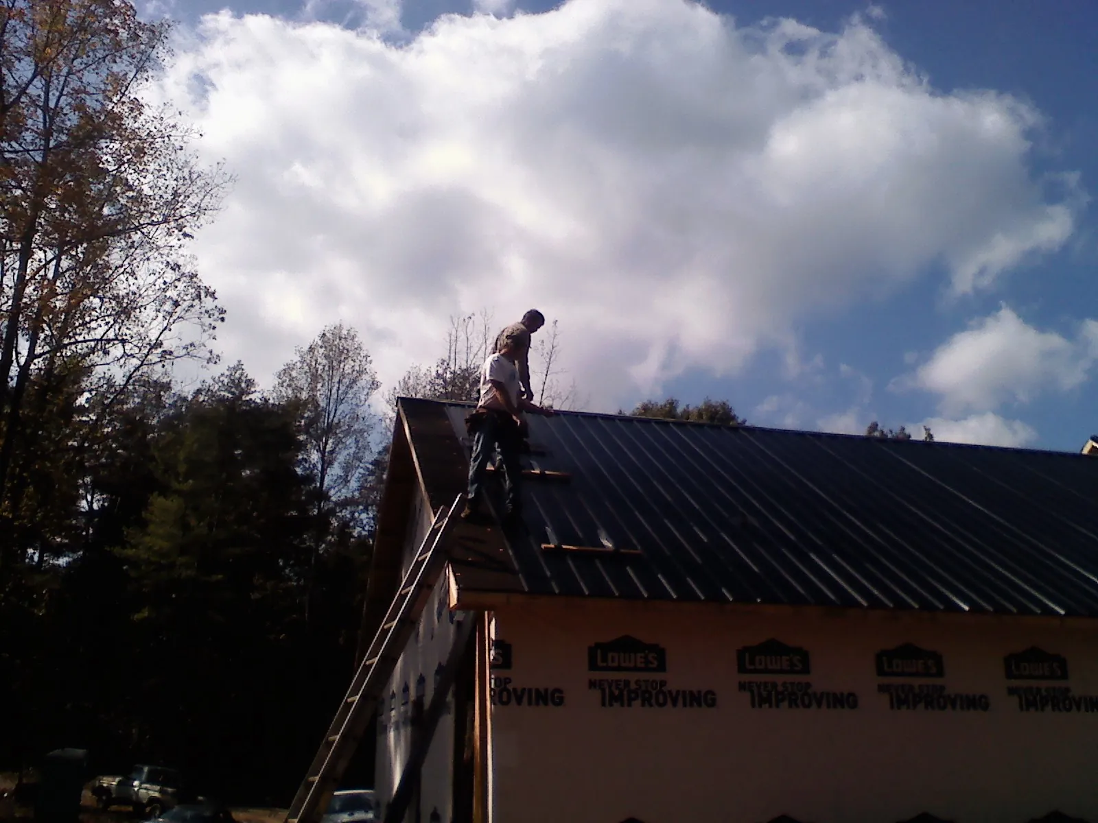 Roofer fastening dark metal panels high against a cloudy sky, from a Roof Inspection job in Foosland