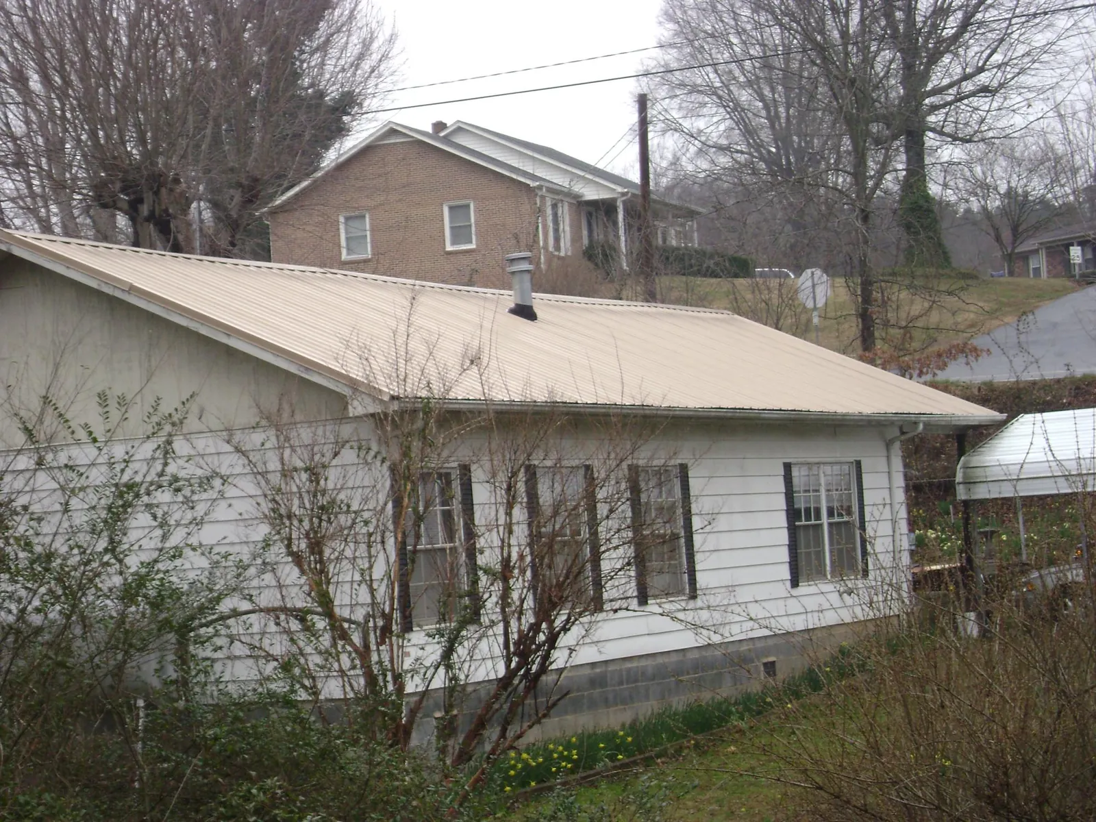 Tan metal roof on a white sided house set into a hillside — Commercial Roofing by Roofing Brothers in Foosland